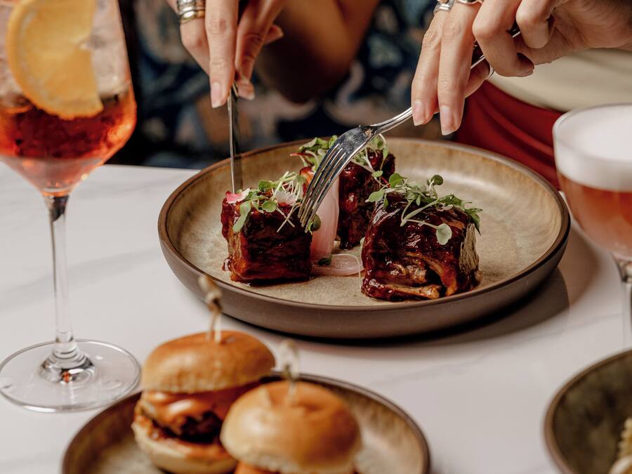 A dining table with a plate of food, a glass of drink, and a burger.