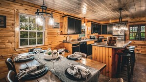 A wooden cabin interior with a dining area set for a meal, a kitchen with modern appliances, and a bar area. - NEW! The Cowboy-5BR Cabin w/HT, Game Room & Pool Access (Sevierville)