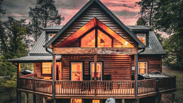 A log cabin with a balcony and a fireplace visible through the windows. - NEW! The Cowboy-5BR Cabin w/HT, Game Room & Pool Access (Sevierville)