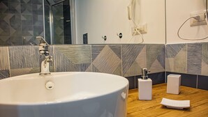 Une salle de bain moderne avec un grand lavabo blanc, un plan de toilette en bois et un revêtement mural en carreaux à motifs géométriques.