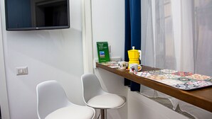 A hotel room with a TV mounted on the wall, a small table with a colorful placemat, two white chairs, a green map, and a yellow mug. - Inner Naples (Naples)