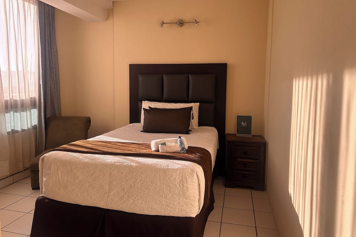 Une chambre d’hôtel avec un lit, une table de chevet, une chaise et une fenêtre avec des rideaux.