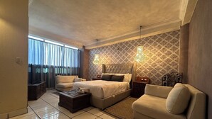 A spacious bedroom with a large bed, a sofa, and a television. - Hotel Miralvalle (San Pedro Sacatepequez)