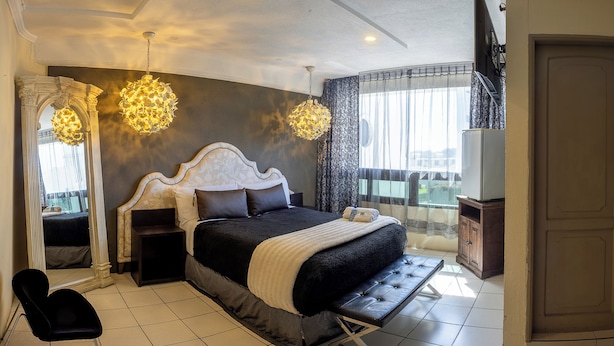 A bedroom with a large bed, a bench, a TV, and a balcony with a view. - Hotel Miralvalle (San Pedro Sacatepequez)