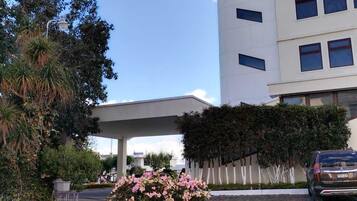 Un edificio moderno con un acceso cubierto, rodeado de vegetación y un coche estacionado.