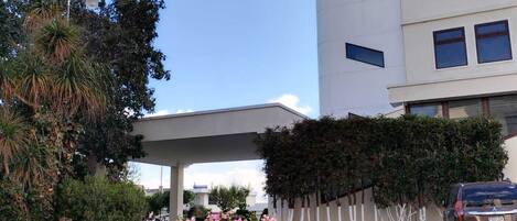 Un edificio moderno con un acceso cubierto, rodeado de vegetación y un coche estacionado.
