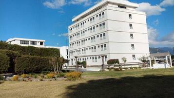 A multi-story white building with a flat roof, surrounded by a well-maintained lawn and some trees.