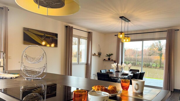 A modern dining area with a central island, a hanging light fixture, and a view of the outdoors. - La Maison du Pinier – Nature (Royères)