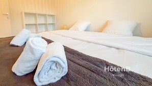 A hotel room with a neatly made bed, a brown rug, and two rolled towels on the floor. - La Maison du Pinier – Nature (Royères)