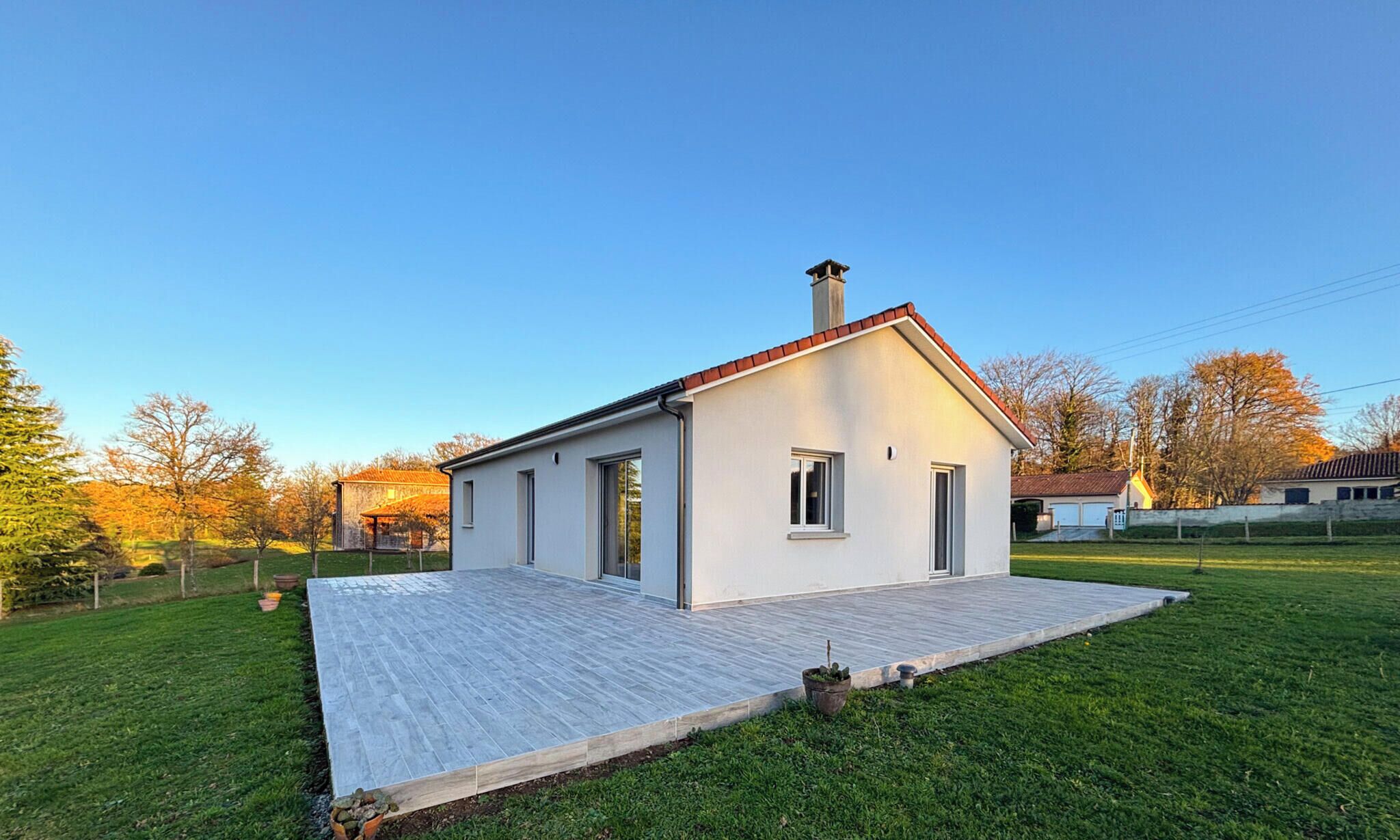 A modern single-story house with a flat roof, a chimney, and a paved patio.