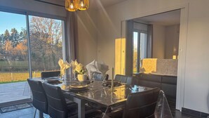 A modern dining area with a glass table, black chairs, and a view of a park. - La Maison du Pinier – Nature (Royères)