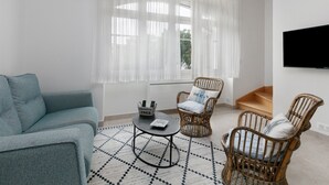 A living room with a sofa, two wicker chairs, a coffee table, and a TV mounted on the wall.