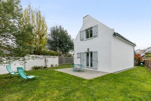 Une maison moderne à l’extérieur blanc, dotée d’un patio avec une table et des chaises, ainsi que d’un petit jardin.