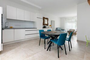 Une cuisine moderne avec des meubles blancs, un coin repas avec des chaises bleues et une table à manger.