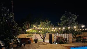 Área de estar ao ar livre com piscina, luzes de cordão e assentos.
