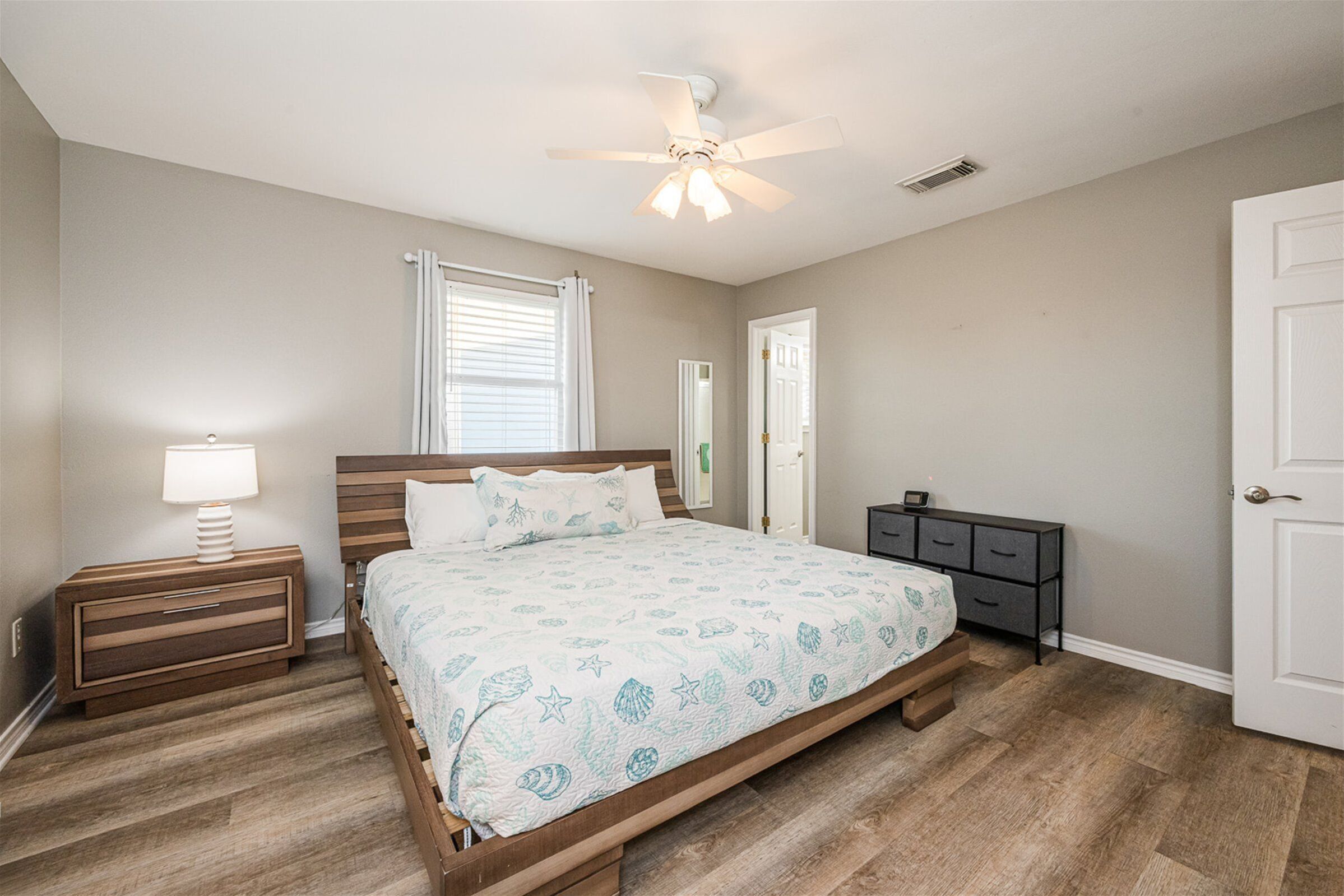 Une chambre à coucher comprenant un lit, des tables de chevet, une commode, un ventilateur de plafond et une porte.