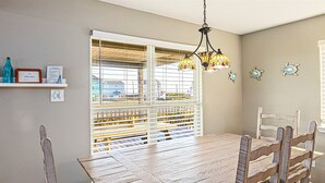 Uma sala de jantar com mesa e cadeiras de madeira, luminária pendente de vitral e janela com persianas.