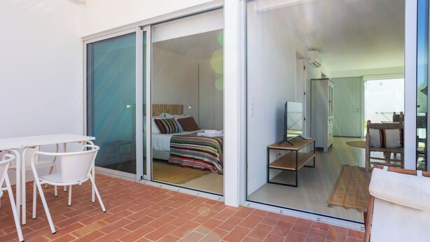 A modern room with a bed, a small table, and a chair. There is a sliding glass door leading to another room. - CASA DO REGADIO - CASA 3, A country and sea retreat on the Alentejo coast, (Beja)