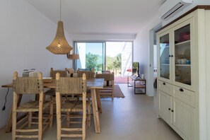 Ein Essbereich mit einem Holztisch und Stühlen, einer geflochtenen Pendelleuchte und einem Schrank mit Glastüren.