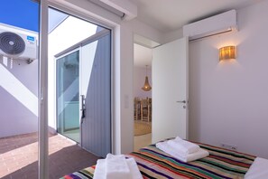 Ein Hotelzimmer mit einer Schiebetür zu einem Außenbereich, einem Bett mit gestreifter Decke, einem Nachttisch und einer Wand-Klimaanlage.