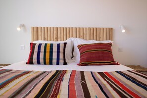 A bed with a striped blanket and two pillows, a wooden headboard, and two wall-mounted lights. - CASA DO REGADIO - CASA 3, A country and sea retreat on the Alentejo coast, (Beja)