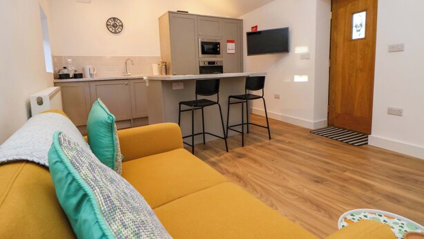 A compact living space with a sofa, a small kitchen area, and a dining table with two chairs. - The Apple Store (Tarporley)