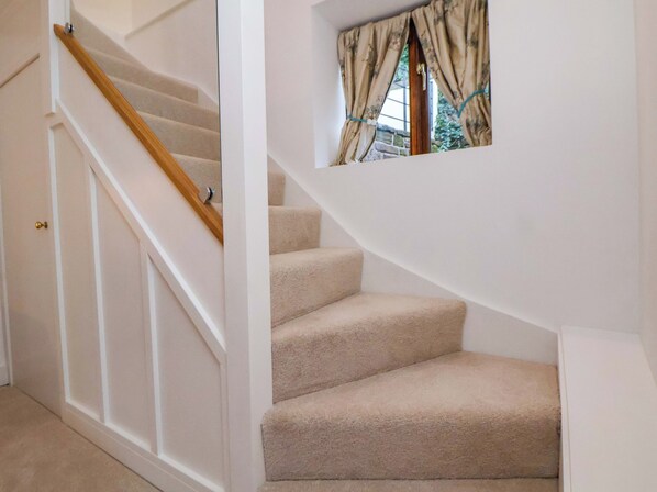 A carpeted staircase with a wooden handrail and a window with curtains.