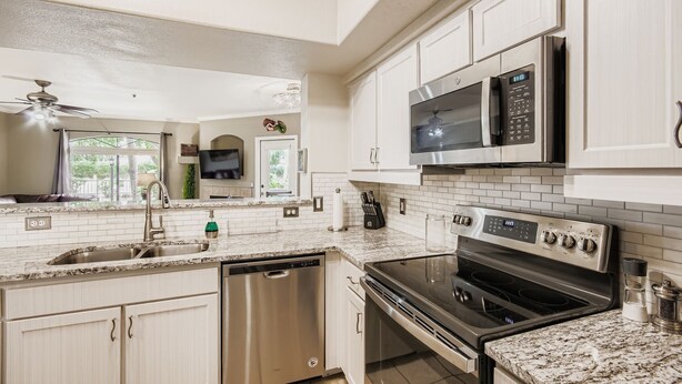 A modern kitchen with white cabinets, a stainless steel dishwasher, an oven, a microwave, and a granite countertop. - 2bd/2ba North Scottsdale Condo (Scottsdale)