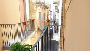 A narrow urban street with a balcony, a potted plant, and a pinwheel decoration.