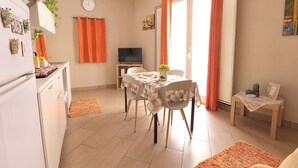 A compact kitchen with a dining area, a TV, and a small table with a vase.