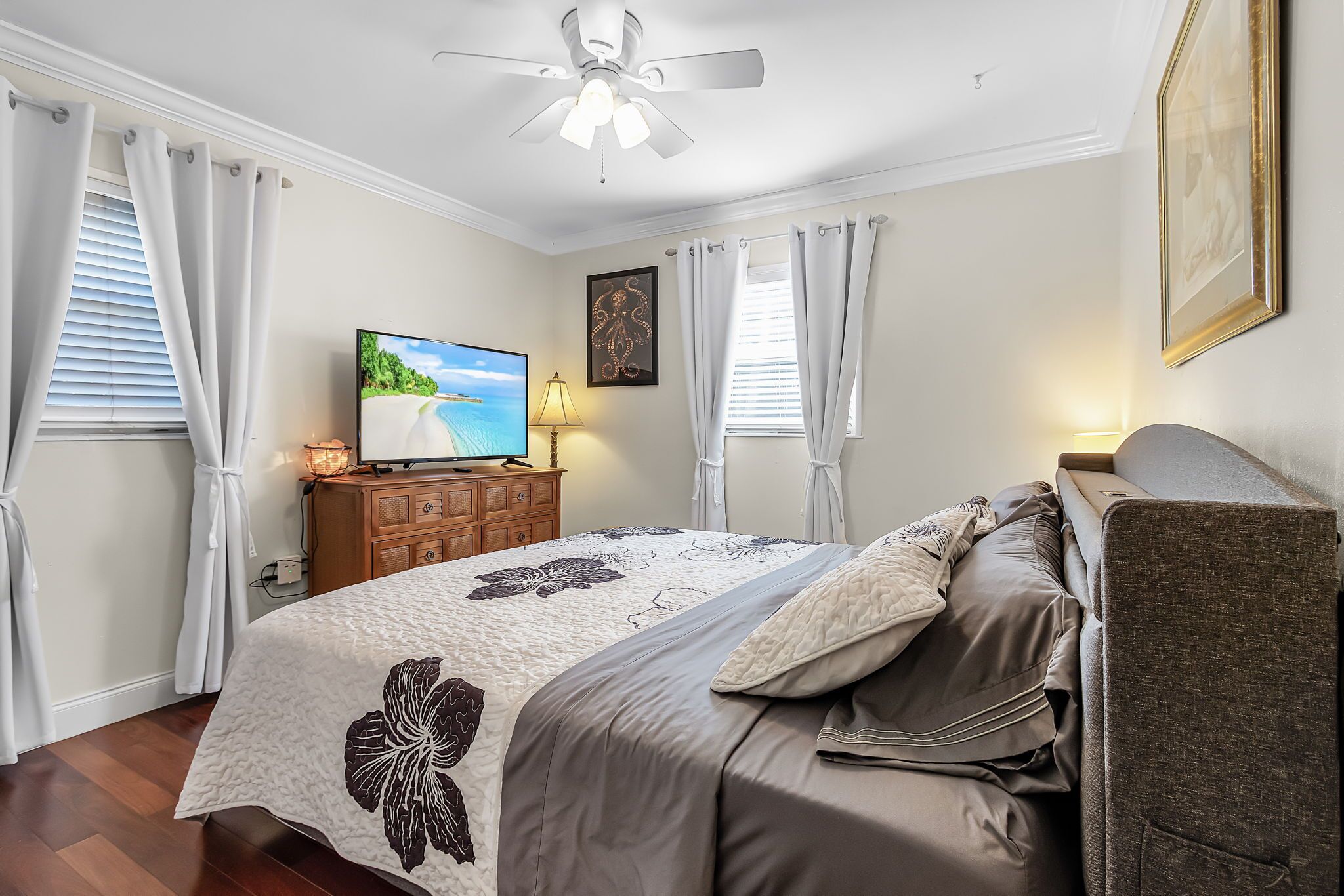 A bedroom with a bed, a television, a ceiling fan, and a dresser.