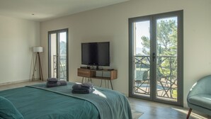 A bedroom with a bed, a TV on a stand, a floor lamp, and a sliding glass door leading to an outdoor area. - La Villa Ange - Villa 10 pers avec piscine à Puget (Puget)