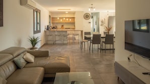 A modern living room with a sofa, a coffee table, and a TV. There is a kitchen in the background with a dining area. - La Villa Ange - Villa 10 pers avec piscine à Puget (Puget)