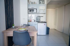 A compact kitchen with a microwave, sink, and small refrigerator. There is a dining table with chairs and a potted plant. - Bail mobilité - Beau studio proche tram Saint-Roch (Nice)