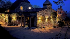 A stone house with a steeply pitched roof, a central chimney, and a small tower-like structure.
