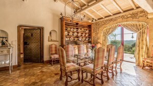 A dining area with a glass table and chairs, a wooden cabinet with dishes, and a stone wall with a window.