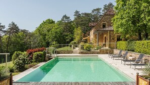 A swimming pool with lounge chairs, a stone building, and a forested backdrop.