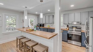 Una cocina moderna con armarios grises, electrodomésticos de acero inoxidable y una isla de madera con taburetes.