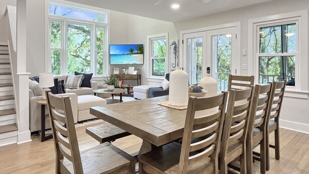 Un salón amplio con una mesa de comedor, sillas, un sofá y un televisor montado en la pared.