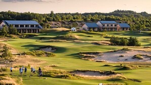 En golfbane med bunkers, en klubhus og en gruppe mennesker der spiller.