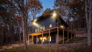 A two-story cabin with a balcony, surrounded by trees. - Family Friendly Modern Cabin w/ Hot Tub, Fire Pit & EV Charger - Lost River WV (Lost City)