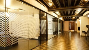 Un interior moderno con divisiones de vidrio, suelo de madera y techo con vigas y luces a la vista.