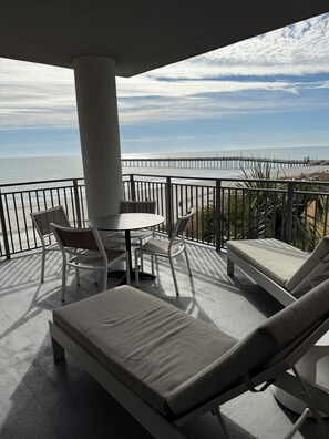 A balcony with a table and chairs, a lounge chair, and a view of the ocean and pier. - Rare, Luxury, 3 Bedroom/2 Bathroom Oceanfront Condo in Myrtle Beach, SC (Myrtle Beach)