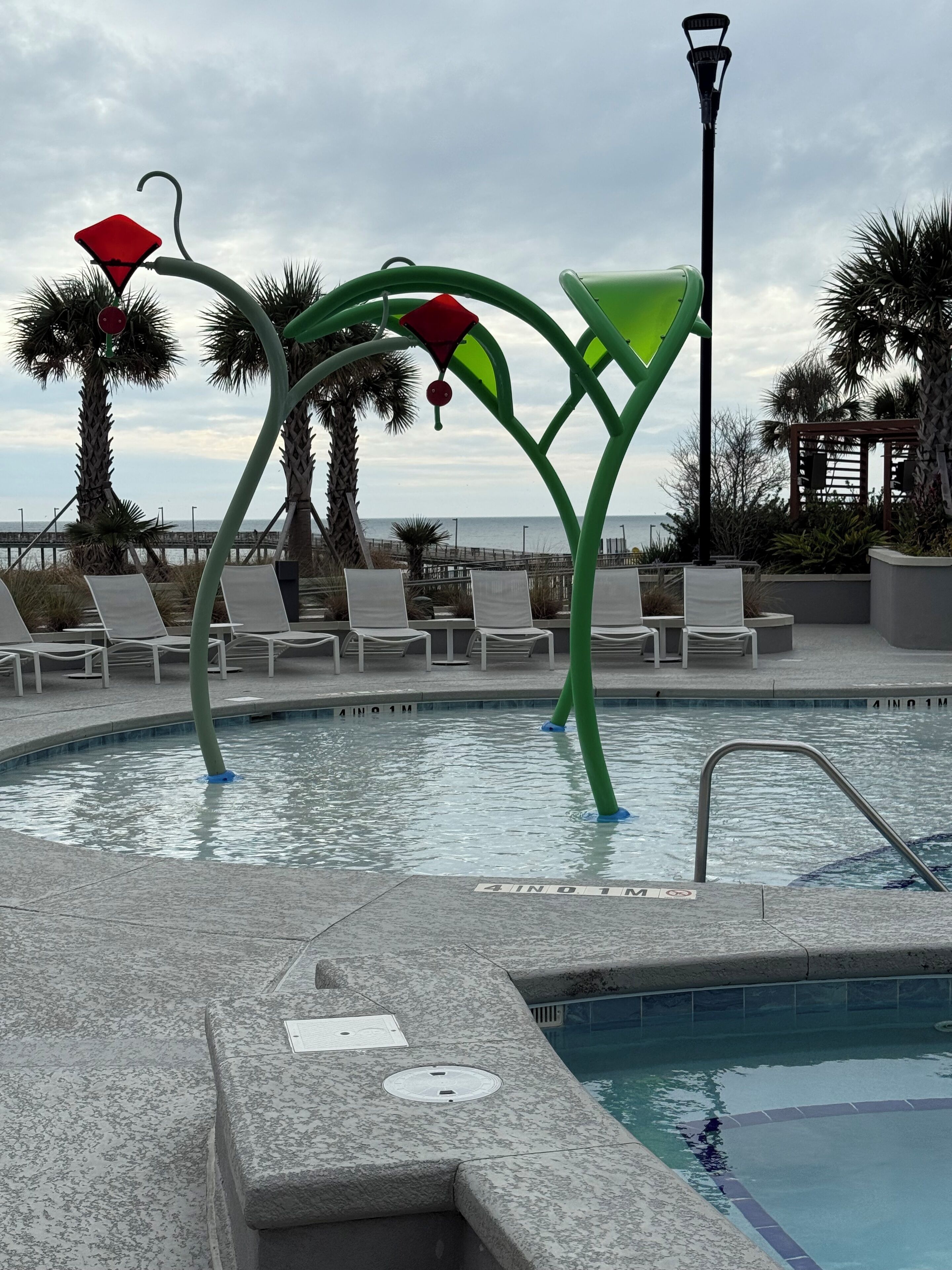 A pool area with lounge chairs, a decorative metal structure, and a view of the ocean.