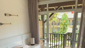 Une chambre à coucher avec un lit, des oreillers, une table de chevet avec une lampe, et une vue sur le balcon extérieur.