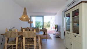 Un coin repas comprenant une table et des chaises en bois, un luminaire suspendu en fibres tressées et un meuble avec des portes en verre.