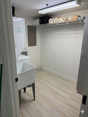 Une pièce avec un réfrigérateur blanc, un évier blanc, une étagère avec du papier toilette et une porte dotée d’une poignée.