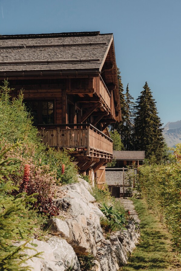 A wooden chalet with a balcony, surrounded by greenery and rocks. - MAISON DOMINOS Chalet de Luxe, 5 chambres, Vue Mont Blanc, Spa, Jacuzzi, Salle de sport (Saint-Gervais-les-Bains)