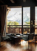 Una stanza con pavimento in legno, vista sulle montagne, un balcone in legno esterno e una finestra con tende.