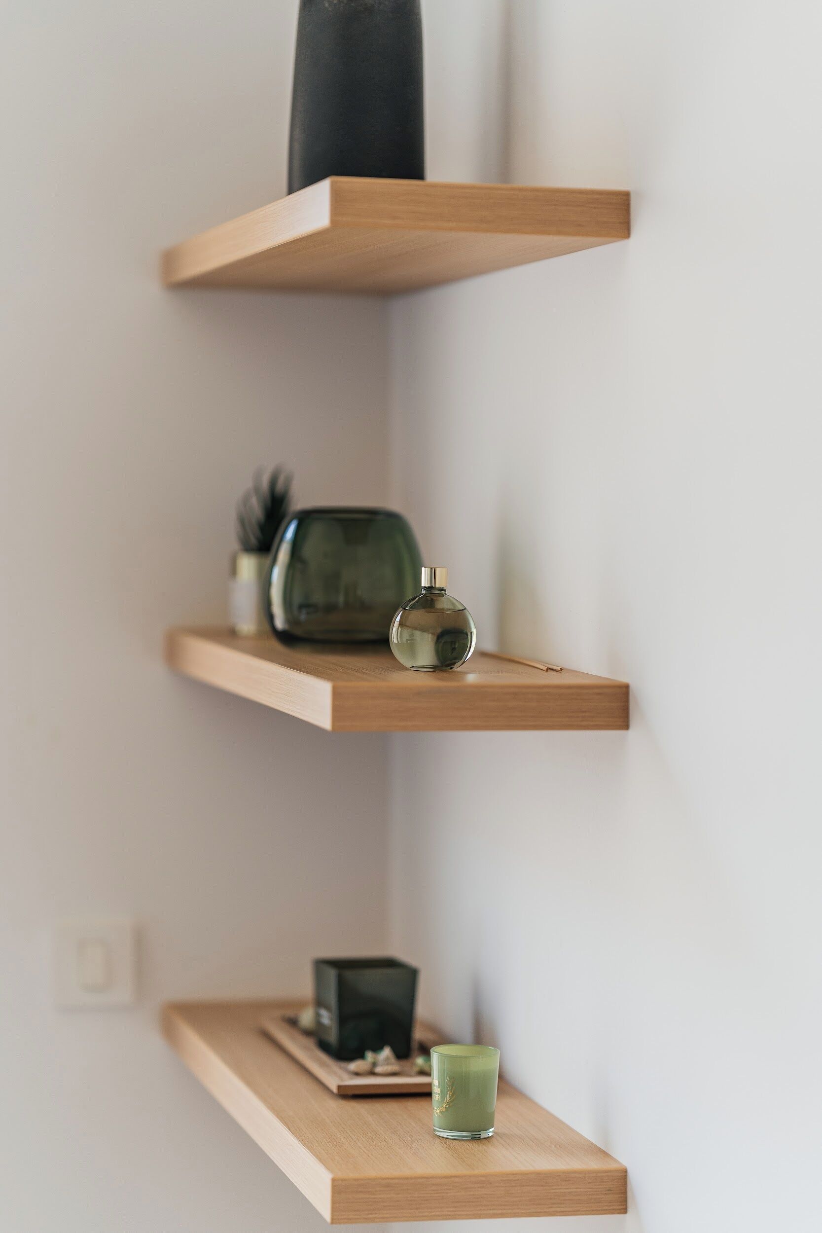 En minimalistisk hylla med en liten växt, en dekorativ detalj och en glasbehållare.